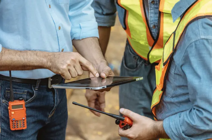 a man in a blue shirt is showing to men in high-visibility vests something on his tablet