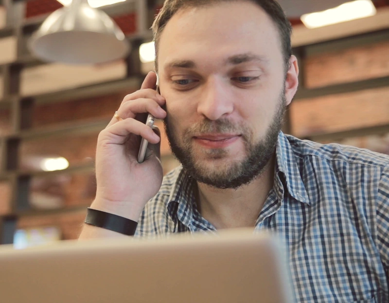 A man speaks on the phone while focused on his laptop screen, engaged in a conversation and work simultaneously.